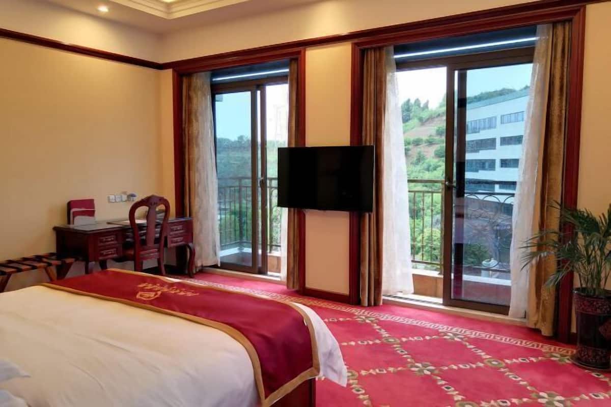 Habitación de hotel con cama, escritorio, silla, televisor y balcón con vistas al exterior.
