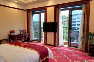Habitación de hotel con cama, escritorio, silla, televisor y balcón con vistas al exterior.