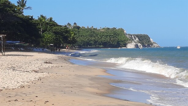 Une plage aux eaux cristallines, un rivage sablonneux et une falaise boisée.