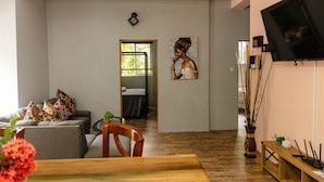 A modern living room with a sofa, a dining table, and a TV mounted on the wall. - TOPAZ APARTMENT VILLA -  MOUNTAIN VIEW VILLA (SOUFRIERE)