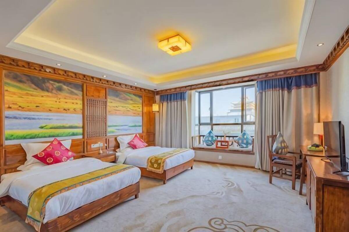 Camera d'albergo con due letti, un'ampia finestra vista e una scrivania con sedia, oltre a una televisione.