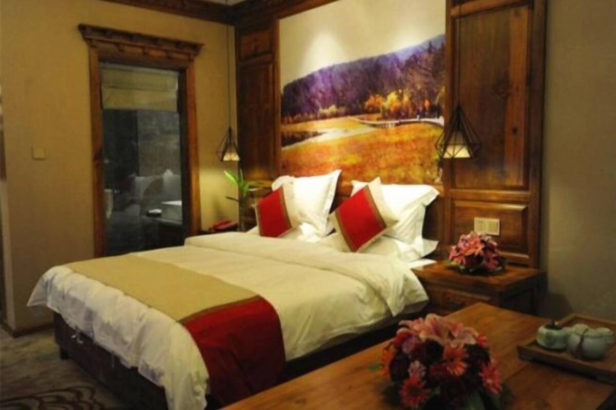 Una camera d'albergo con un letto, una testiera in legno, un quadro appeso al muro, un comodino con una lampada e un bouquet di fiori.