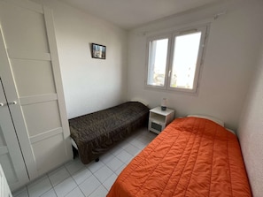 Two single beds, a nightstand with a lamp, and a wardrobe are featured in this cozy room.