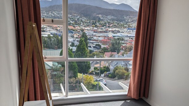 A bedroom with a large window, a bed with patterned bedding, and a wooden easel.