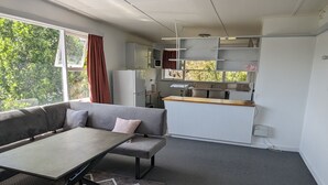A compact living space with a sofa, a small table, a kitchenette, and a view of greenery outside.