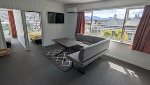 A modern hotel room with a grey sofa, a small table, and a TV mounted on the wall.