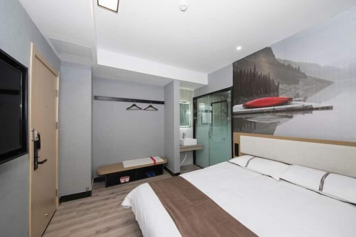 A hotel room with a bed, a bench, a mirror, and a wall-mounted TV.
