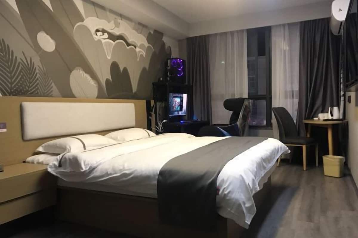 A hotel room with a bed, a desk, a chair, a TV, and a window with curtains.