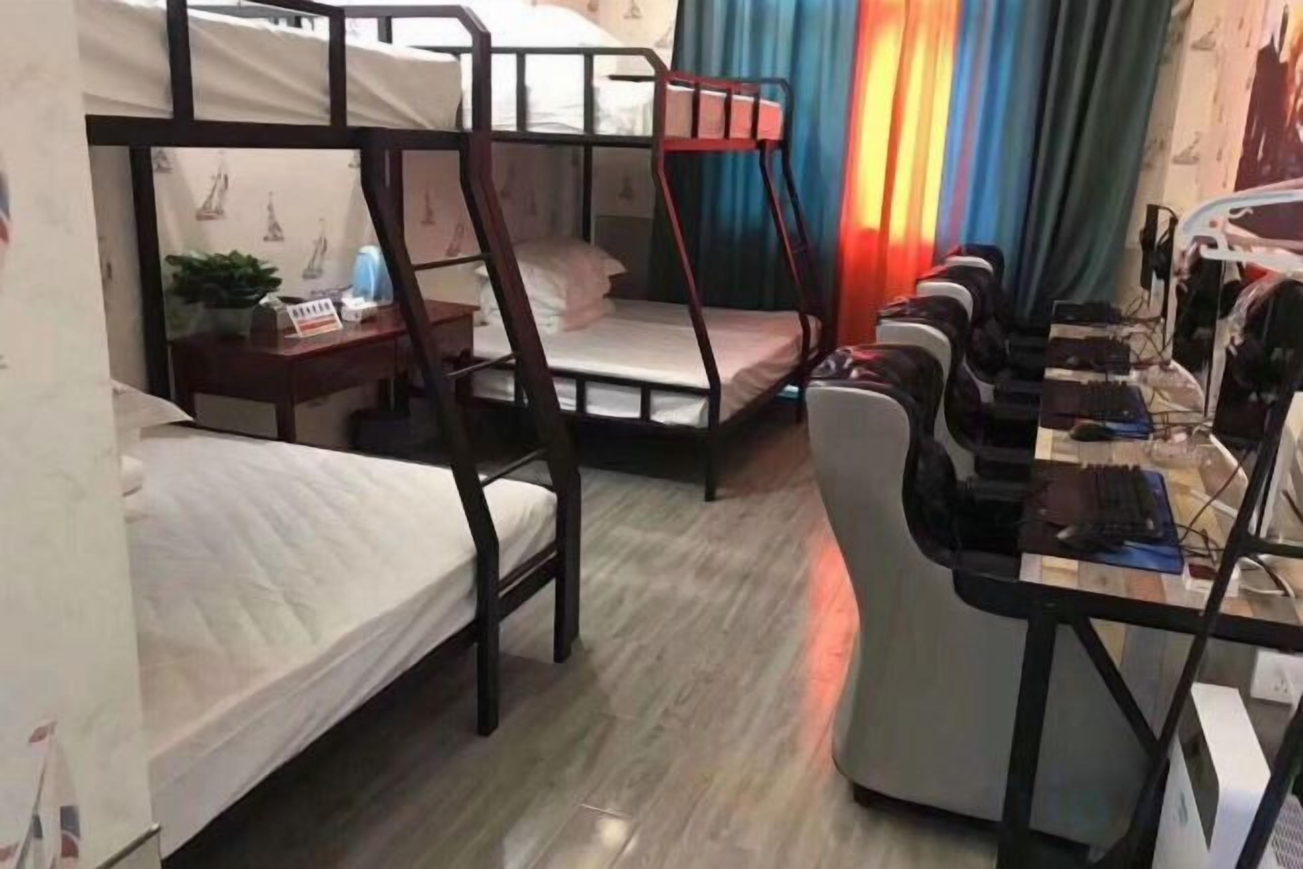 A dormitory room with bunk beds, a desk with a computer, and a window with curtains.