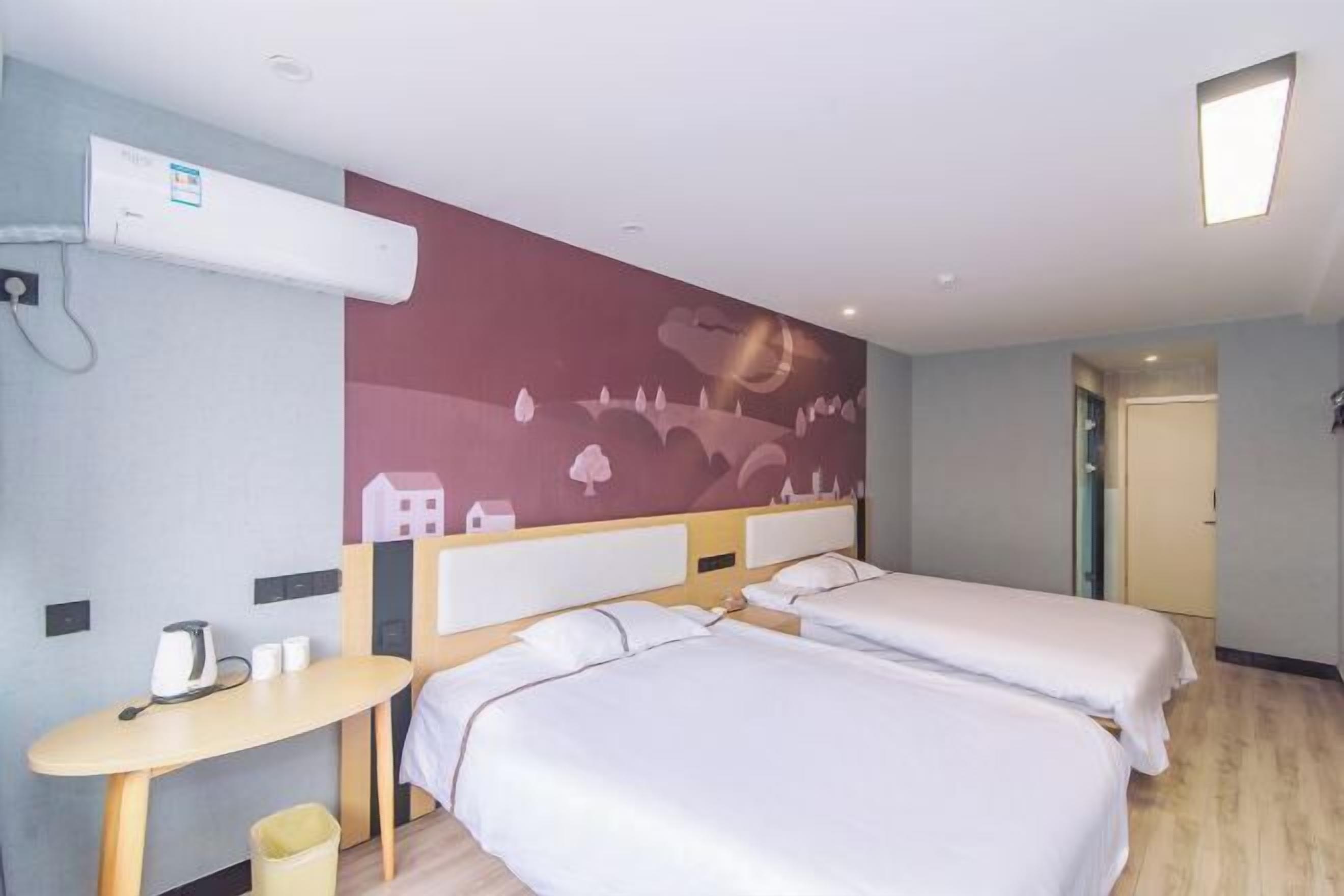 Quarto de hotel com duas camas, uma mesa pequena, ar condicionado fixado na parede e uma porta que dá para outro quarto.