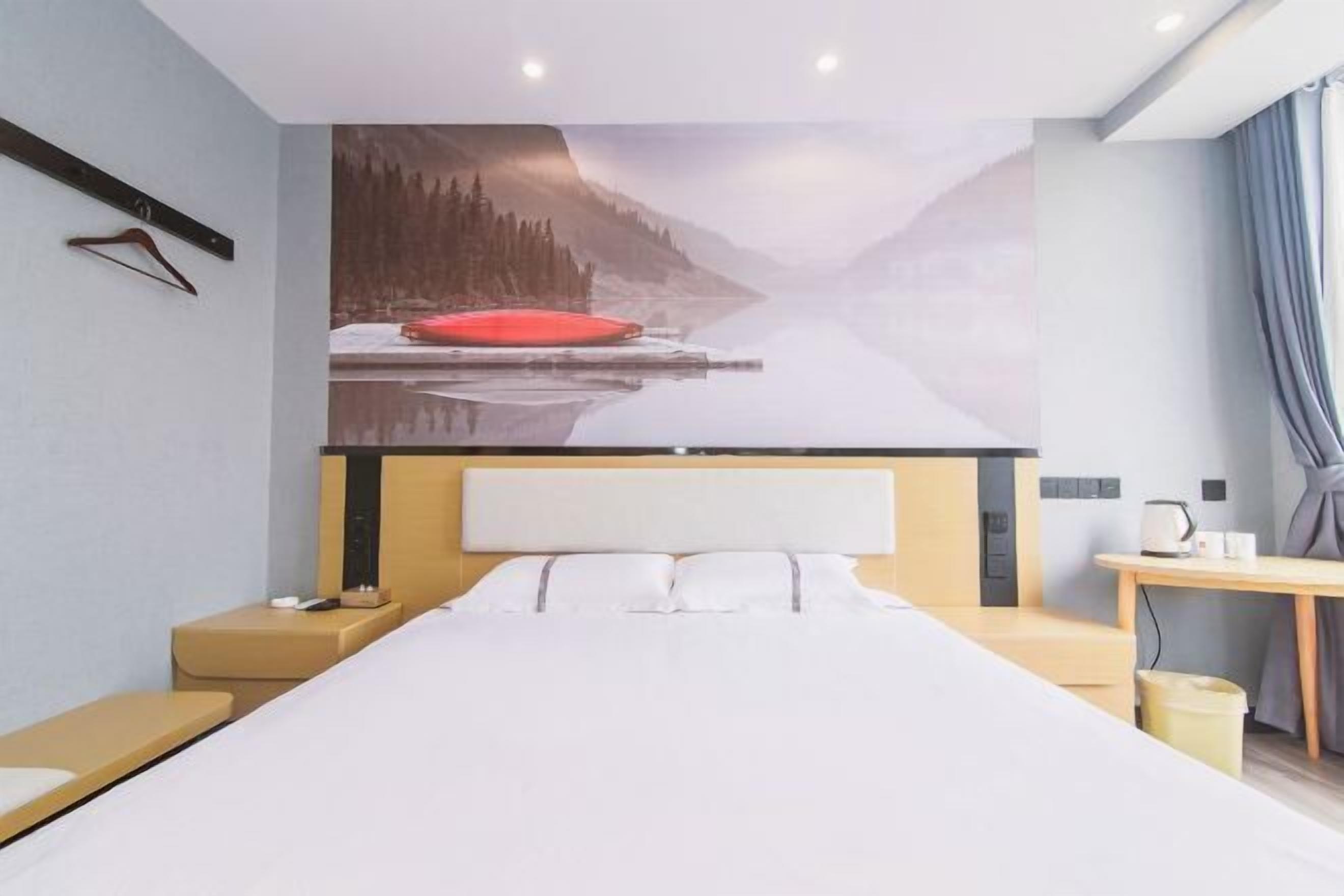 A modern hotel room with a large bed, a bedside table, a nightstand, a wall-mounted TV, and a view of a snowy landscape.