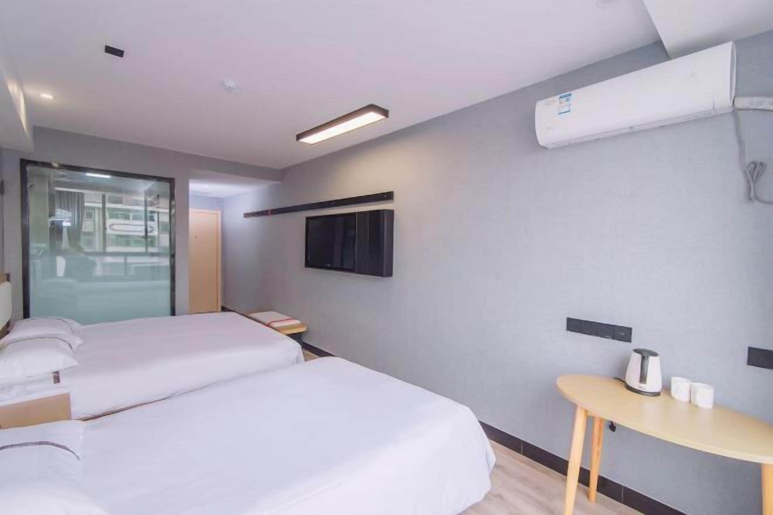 Habitación de hotel con dos camas, una mesita con hervidor y tazas, televisor de pantalla plana en la pared y un equipo de aire acondicionado.
