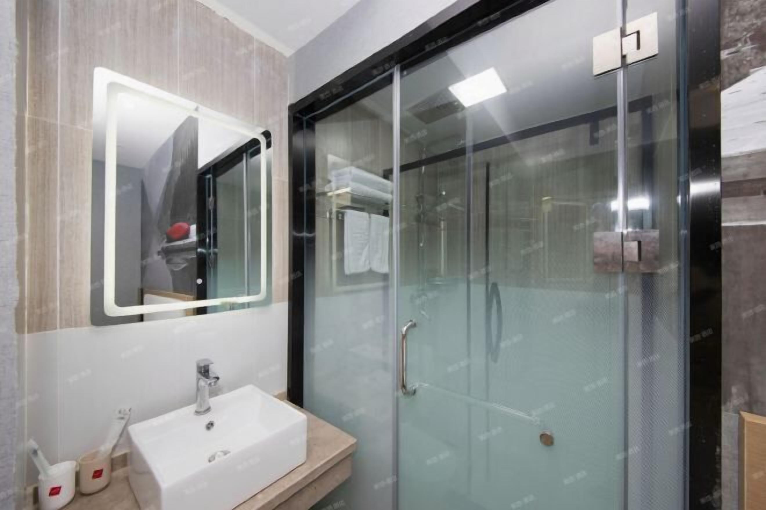 Un baño moderno con ducha envuelta en vidrio, un lavamanos blanco y un espejo con marco iluminado.