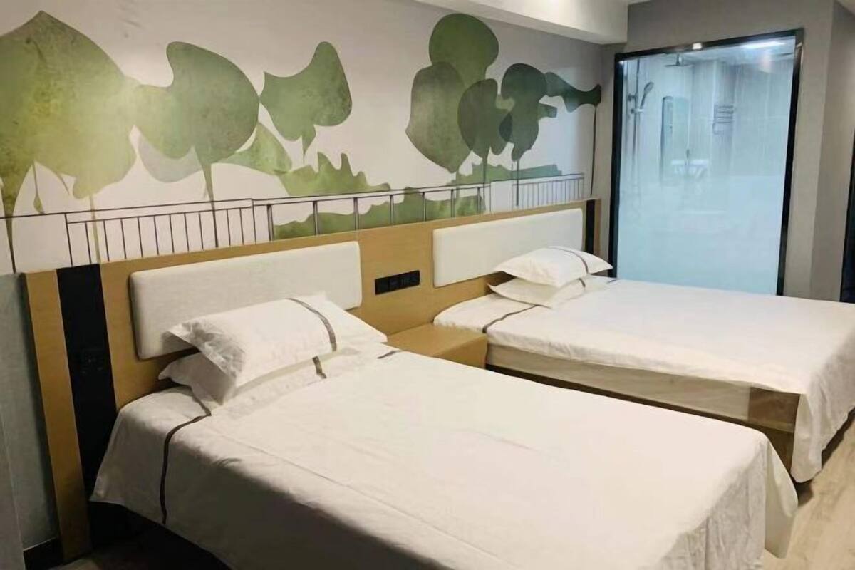 A hotel room with two beds, a wooden headboard, a wall mural, and a glass door leading to a bathroom.