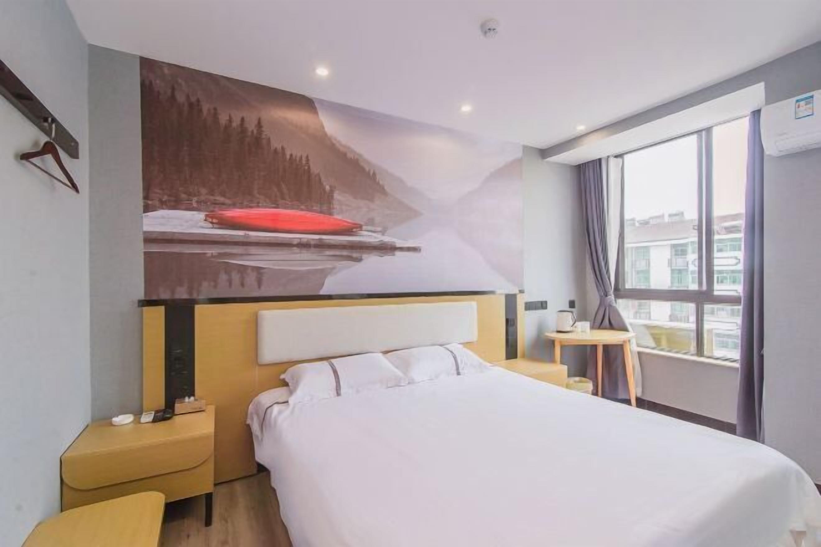 A hotel room with a bed, bedside table, and a painting of a snowy landscape.