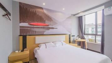 Una habitación de hotel con cama, mesita de noche y un cuadro de un paisaje nevado.