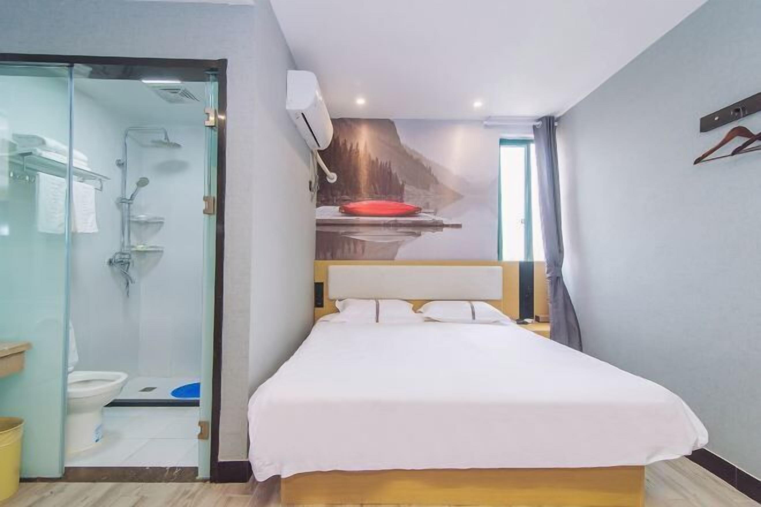 A hotel room with a bed, a shower, a toilet, and a glass door leading to a bathroom.