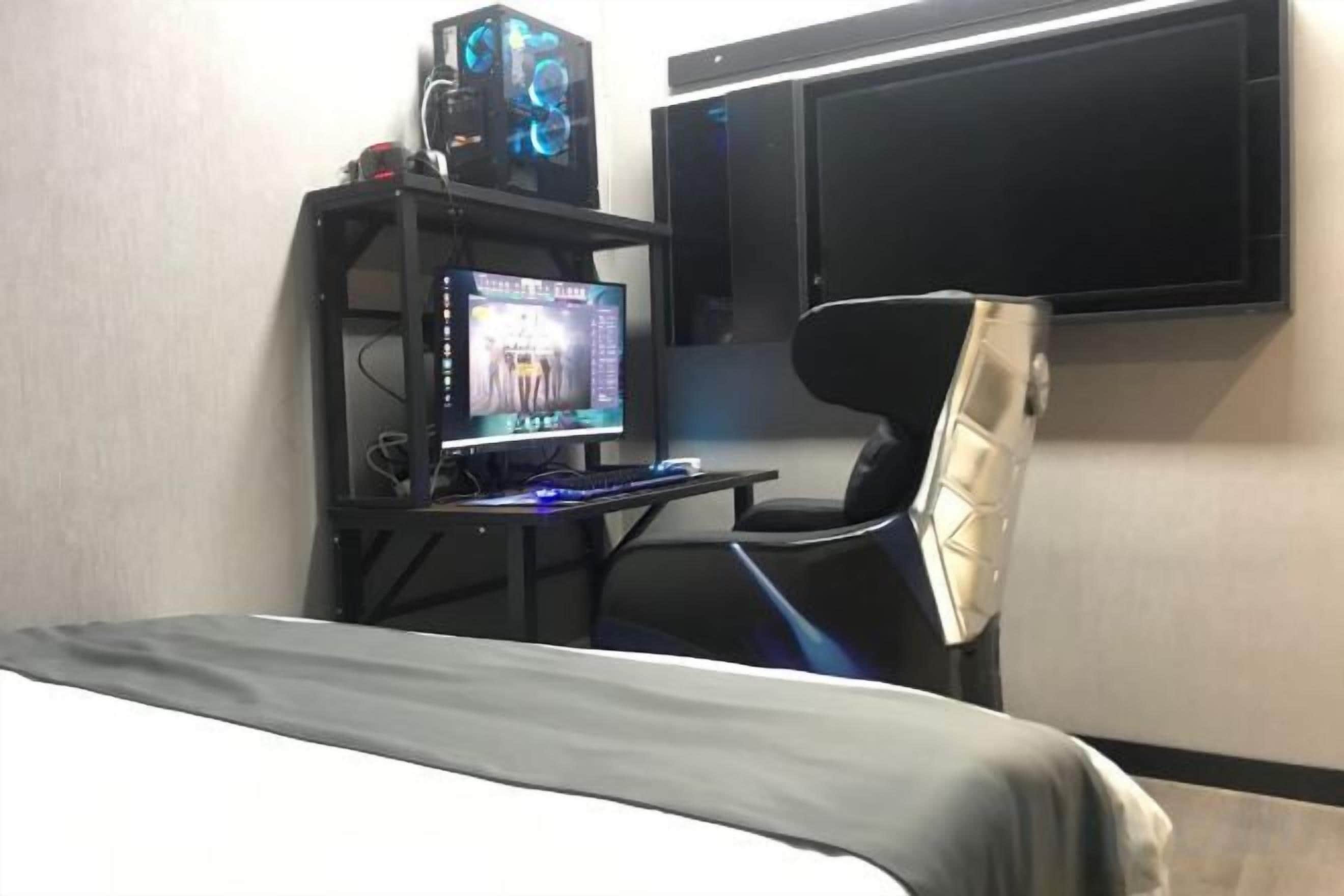 A room with a bed, a desk with a computer, and a TV mounted on the wall.