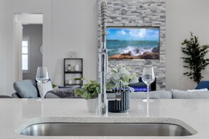 Uma cozinha com uma torneira moderna, duas plantas em vasos e dois copos de vinho no balcão.