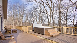 Un terrazzo in legno con posti a sedere all'aperto, una vasca idromassaggio e vista su alberi spogliati.