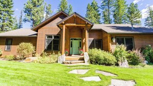 Une cabane en bois avec une porte verte, des marches en pierre et une pelouse bien entretenue.