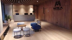 Un área de recepción con un mostrador de madera, varias opciones de asientos que incluyen mesas redondas y sillas, y un logotipo en la pared.