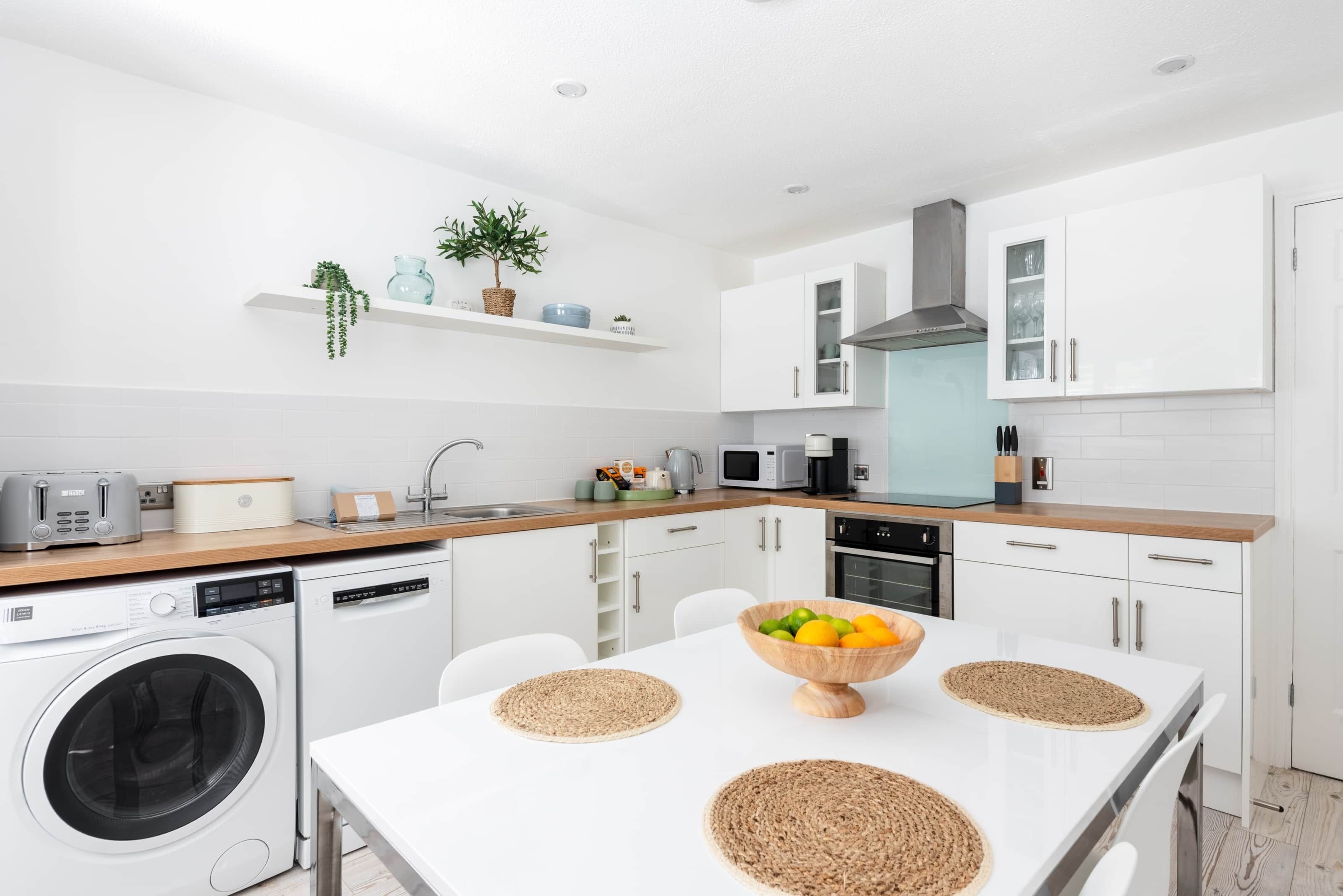 A modern kitchen with white cabinetry, a built-in washing machine, and a dining area with a white table and woven placemats.