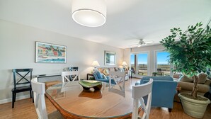 Ein geräumiges Wohnzimmer mit einem Holzessttisch, weißen Stühlen, einem blauen Sofa und einem Topfpflanzen.