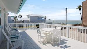 A wooden deck with white furniture, a view of the ocean, and a building with a white facade. - Dog-Friendly Cottage with Ocean Views! Private Heated Pool & Hot Tub! (South Padre Island)