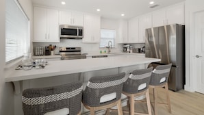 A modern kitchen with white cabinets, stainless steel appliances, and a central island with bar stools. - Dog-Friendly Cottage with Ocean Views! Private Heated Pool & Hot Tub! (South Padre Island)