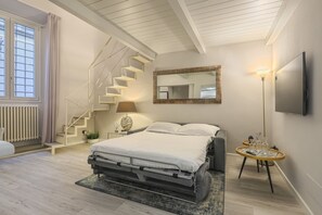 A bedroom with a bed, a staircase, a mirror, a TV, and a small table with items on it.
