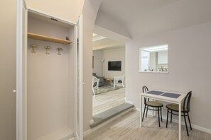 A hallway leading to a dining area with a table and chairs, a coat rack, and a television in the background.