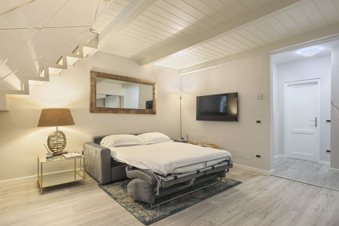 Een slaapkamer met een bed, een bedlampje, een televisie, een spiegel en een trap.