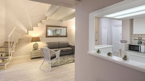 A modern interior with a staircase, a sofa, a chair, a kitchen area, and a large mirror. - Giglio Bianco Apartment (Firenze)