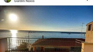 A balcony with a view of the sea and boats, a clear sky, and a building with a tiled roof. - Casa Margot-Giardini Naxos (Giardini Naxos)