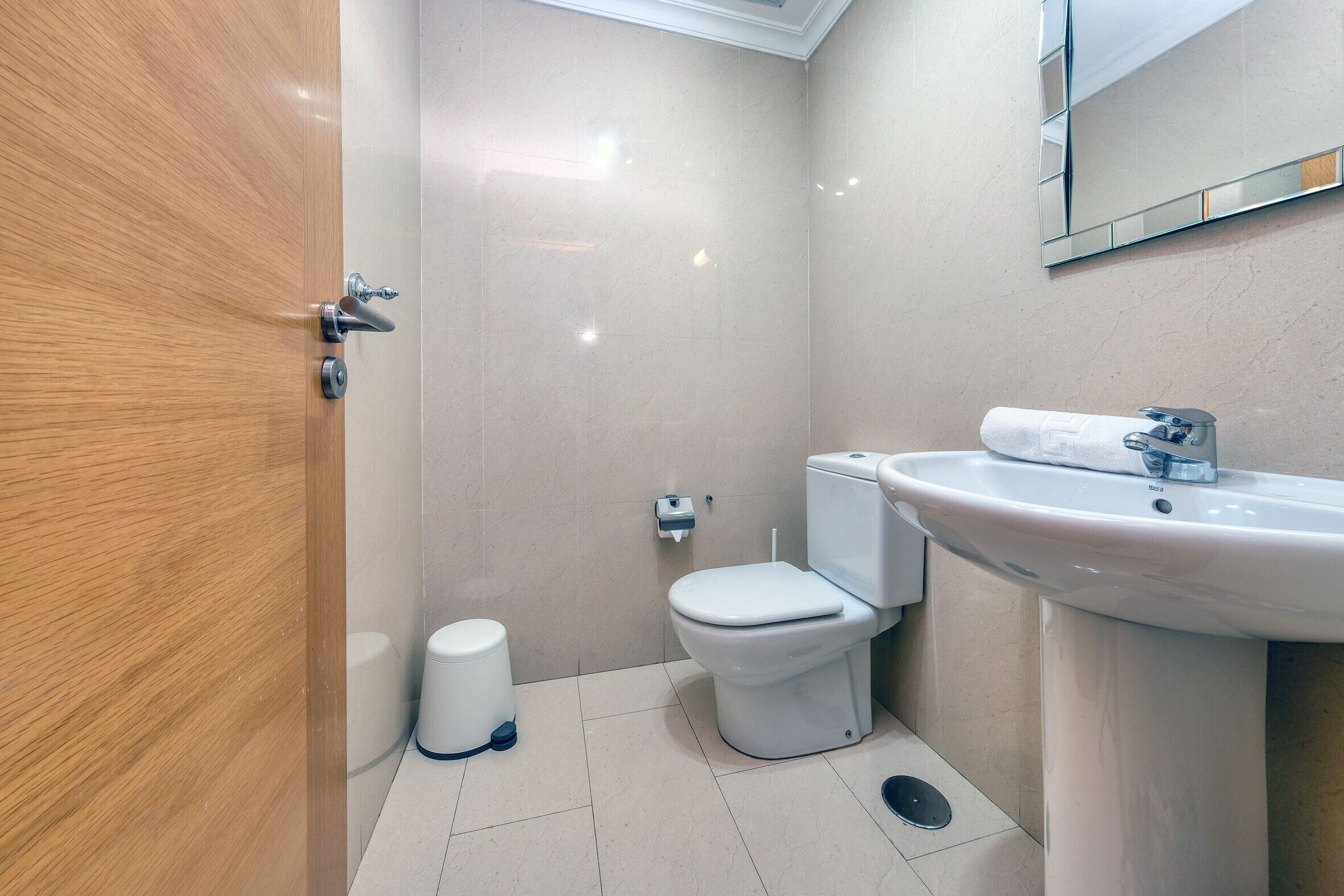 A small, modern bathroom with a wooden door, a white toilet, a sink, and a mirror.