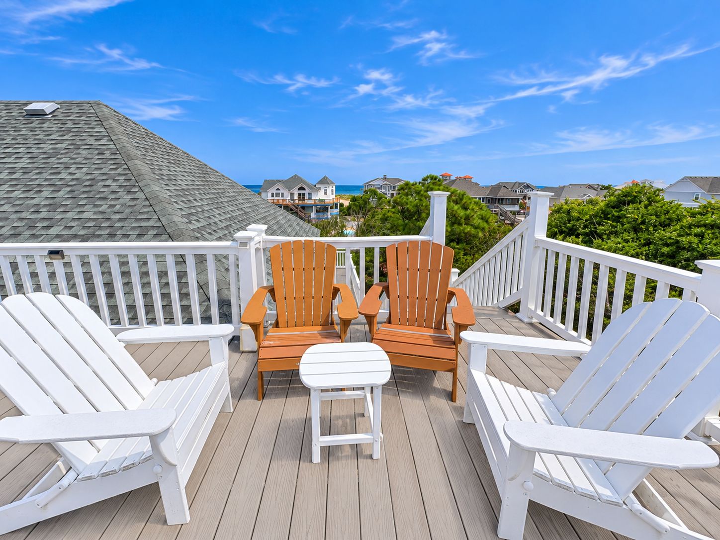A deck with two wooden chairs and a white table, overlooking a residential area with houses and a clear sky.
