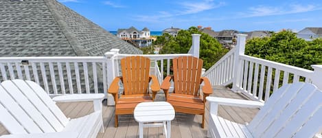 A deck with two wooden chairs and a white table, overlooking a residential area with houses and a clear sky.