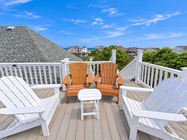 A deck with two wooden chairs and a white table, overlooking a residential area with houses and a clear sky.