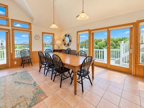 A dining area with a wooden table and chairs, large windows, and a view of the outdoors.