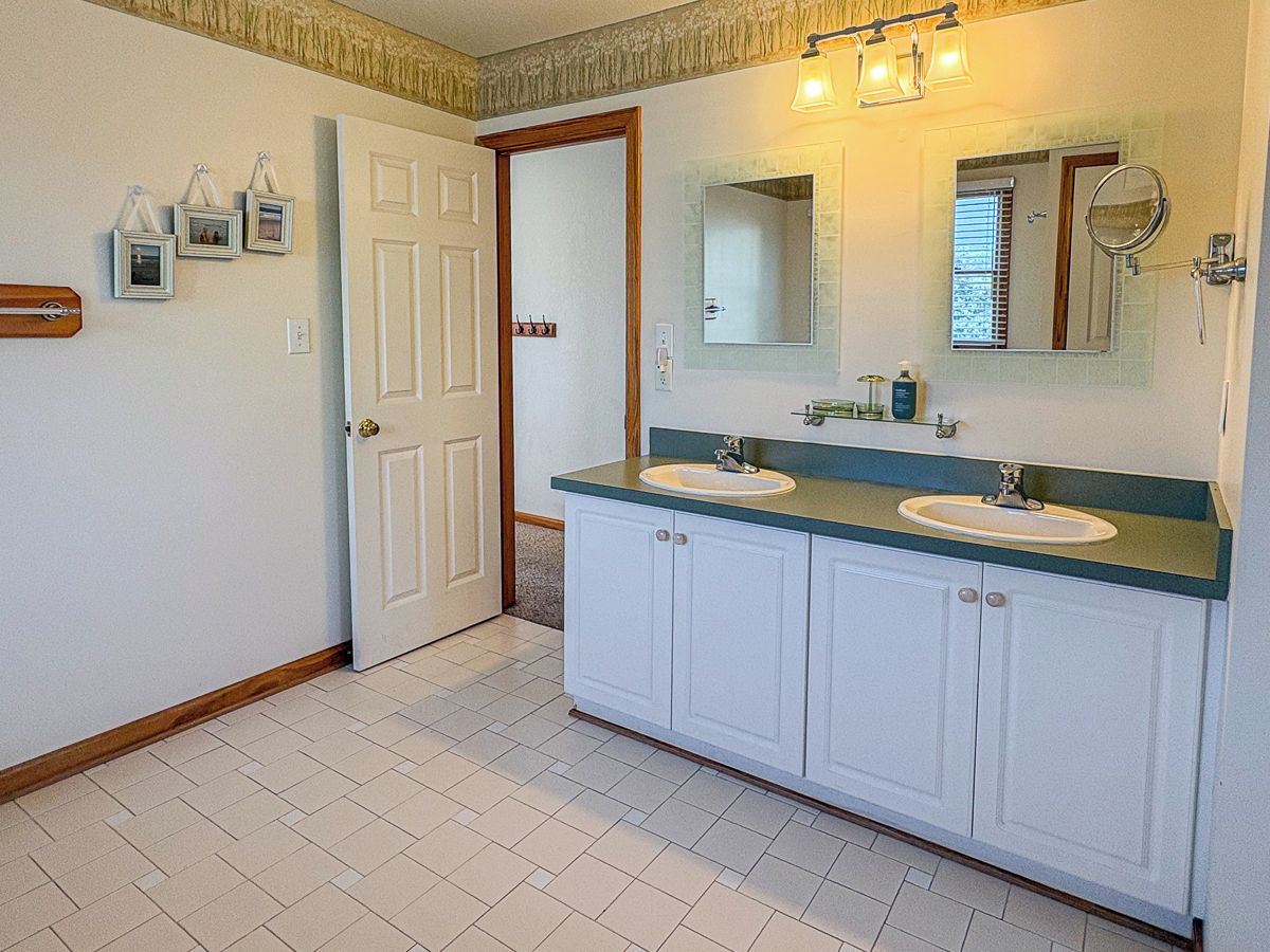 A bathroom with two sinks, a mirror, and a door leading to another room.