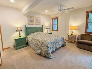A bedroom with a bed, two nightstands, a ceiling fan, a window with blinds, and a brown sofa.