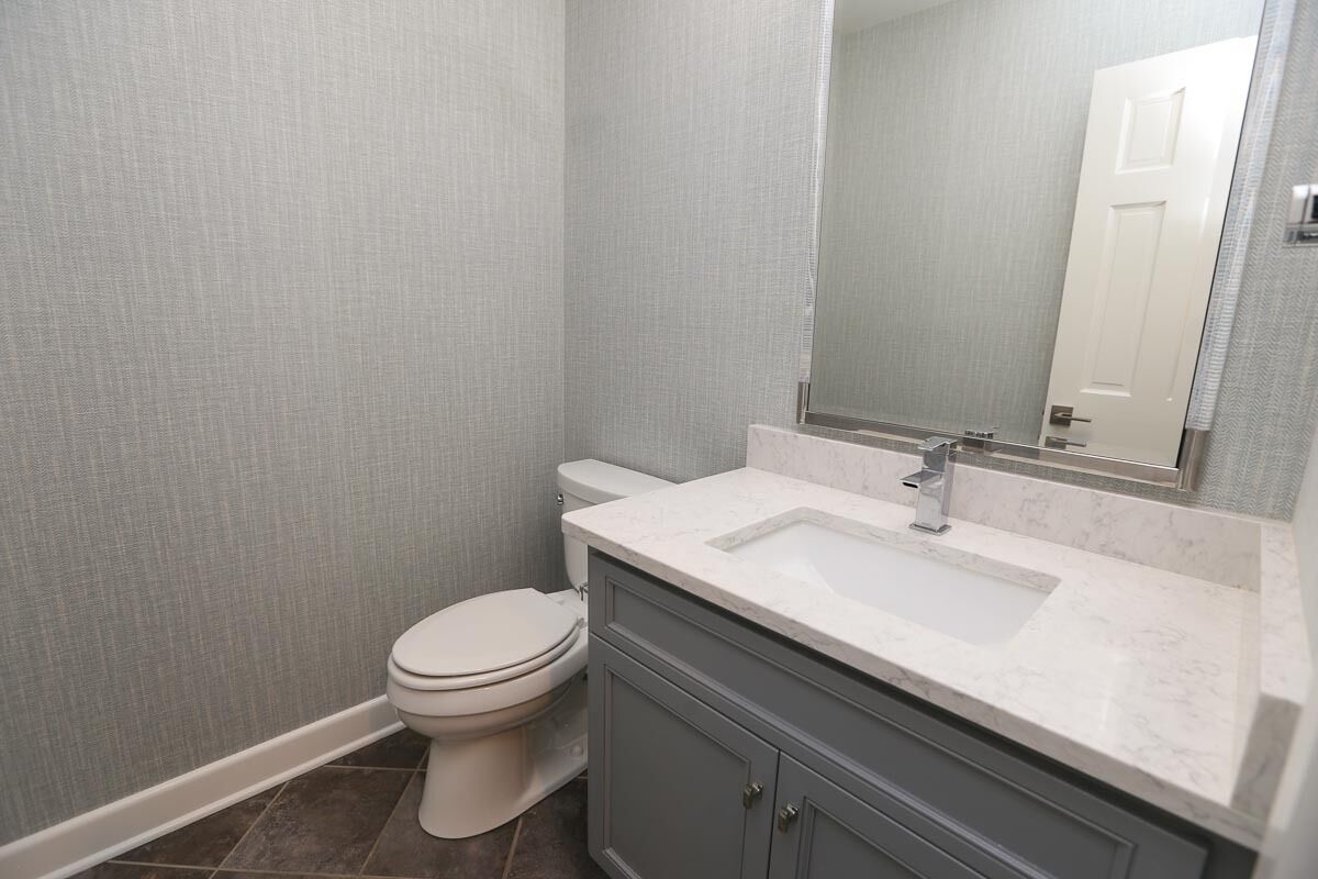 A bathroom with a white toilet, a marble sink, and a gray vanity.