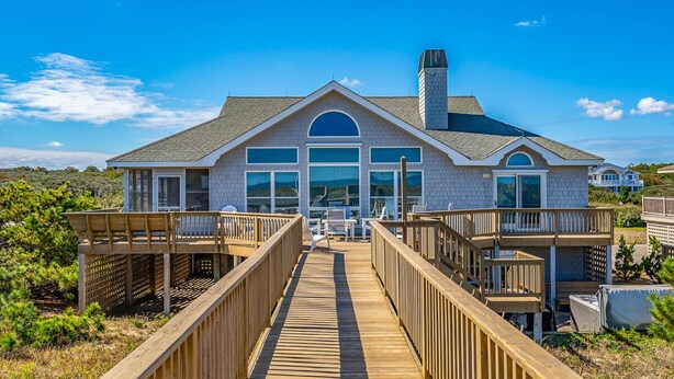 A large house with a wooden deck leading to the entrance, surrounded by greenery. - Baliwest - Gorgeous 5 BR Oceanfront home with a panoramic ocean view! (Southern Shores)