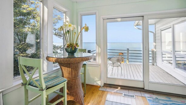 Ein Zimmer mit Meerblick, ein Korbstuhl, ein Tisch mit Blumenvase und eine Glasschiebetür, die auf eine Außenterrasse führt.
