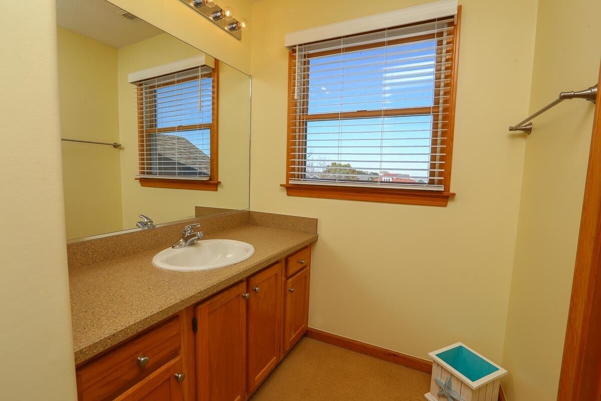 A bathroom with a sink, mirror, wooden cabinets, and a window with blinds.