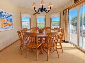 A dining room with a round table, wooden chairs, a chandelier, and large windows.