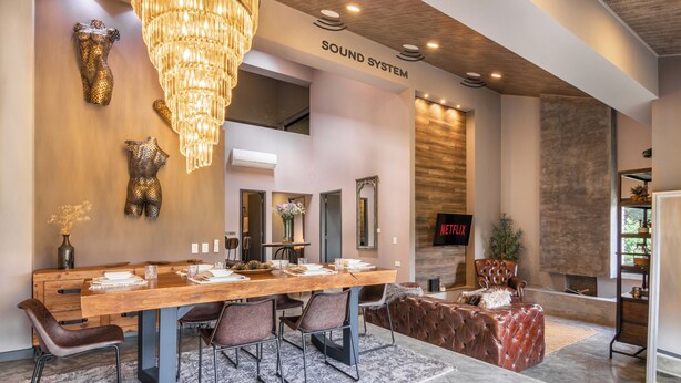A modern interior with a wooden dining table, leather chairs, a chandelier, and a fireplace.