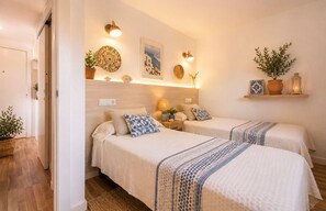 A hotel room with two beds, a wooden headboard, wall-mounted lamps, a shelf with decorative items, and a potted plant.