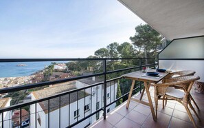 Un balcón con mesa y sillas que da a un pueblo costero y al mar.